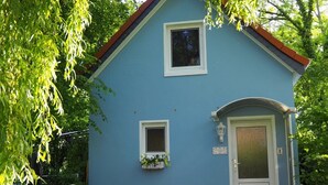 Ein kleines, eingeschossiges Gebäude mit blauer Fassade, einer weißen Tür und einem kleinen Fenster.