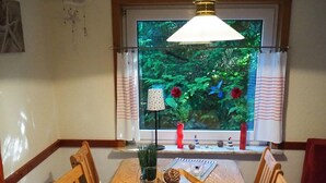Ein Essbereich mit einem Holztisch, Stühlen, einer Hängeleuchte, einem Fenster mit Blick auf Grünflächen und einer Blumenvase.
