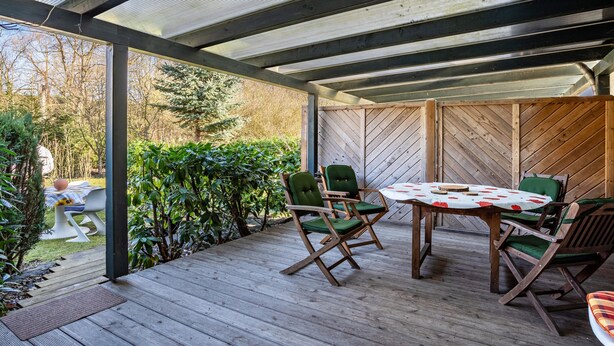 An outdoor patio with a wooden deck, a table with chairs, and a herringbone-patterned wall. - Apartment 'Reinhards' with Private Terrace, Private Garden and Wi-Fi (Greifswald)