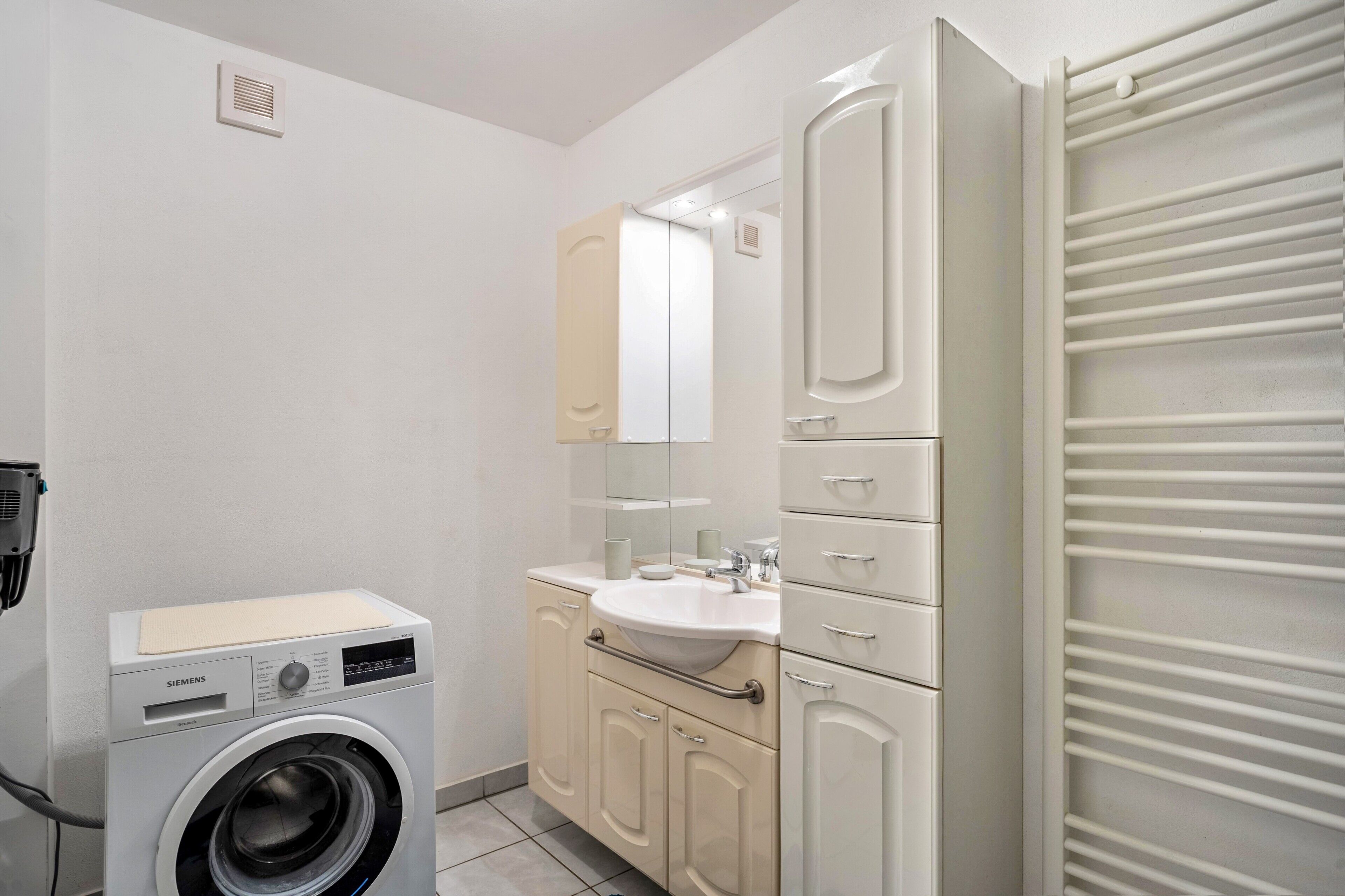 Een kleine badkamer met een wasmachine, een wastafel en een spiegel.
