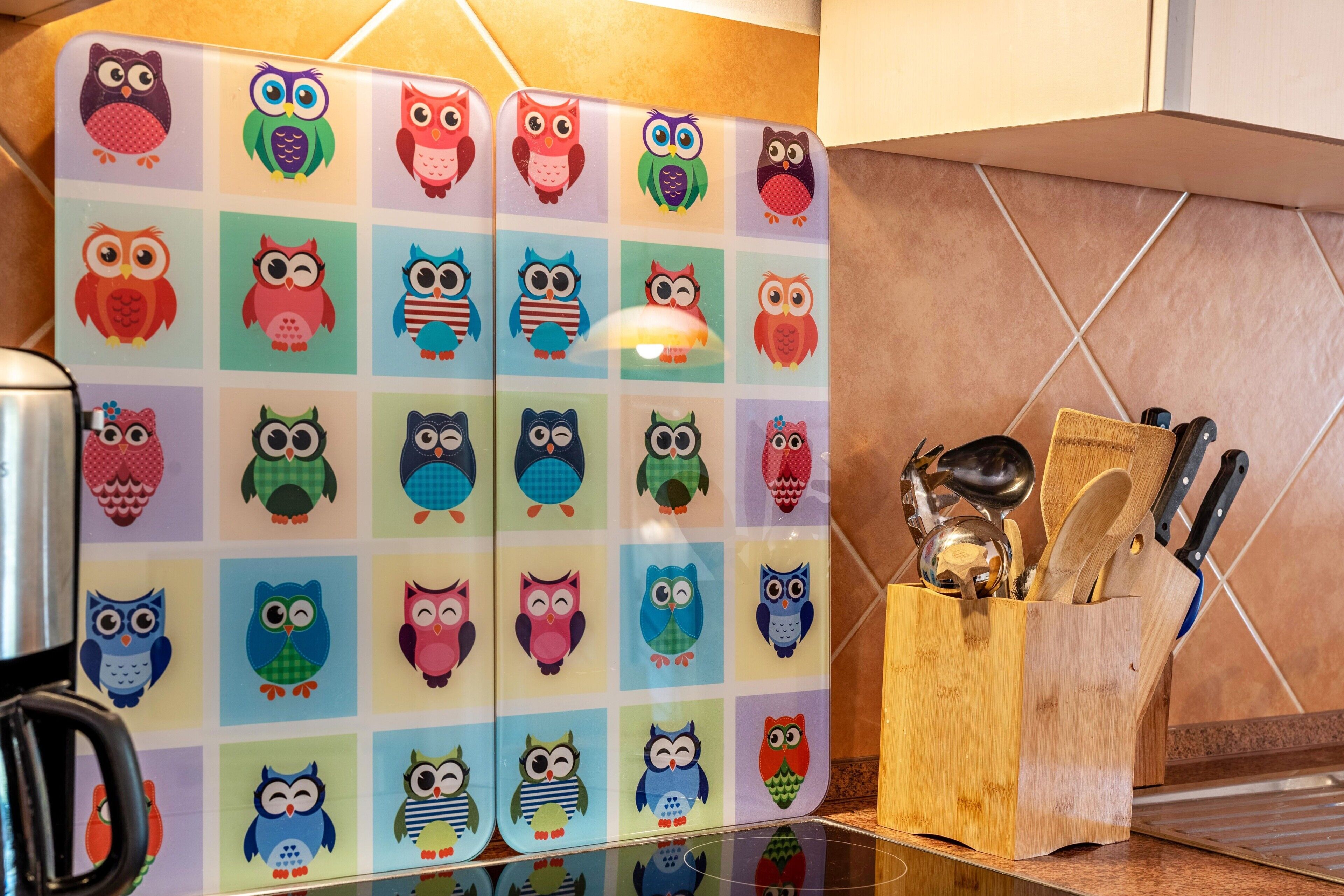 A kitchen with a colorful owl-themed backsplash, a wooden utensil holder, and a kettle.