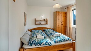 A double bed with patterned bedding, a wooden wardrobe, a shelf with a lamp, and a window with curtains. - Apartment 'Reinhards' with Private Terrace, Private Garden and Wi-Fi (Greifswald)