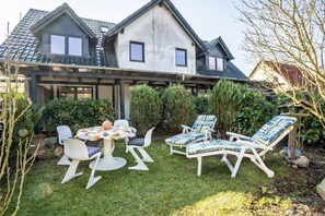 Et hus med en overdækket terrasse, udendørs møbler og en velplejet have.