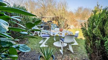 A garden with a table and chairs, surrounded by greenery and trees.