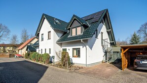 A two-story house with a sloped roof, a visible staircase to the upper floor, and a garage with a car parked inside. - Apartment 'Reinhards' with Private Terrace, Private Garden and Wi-Fi (Greifswald)