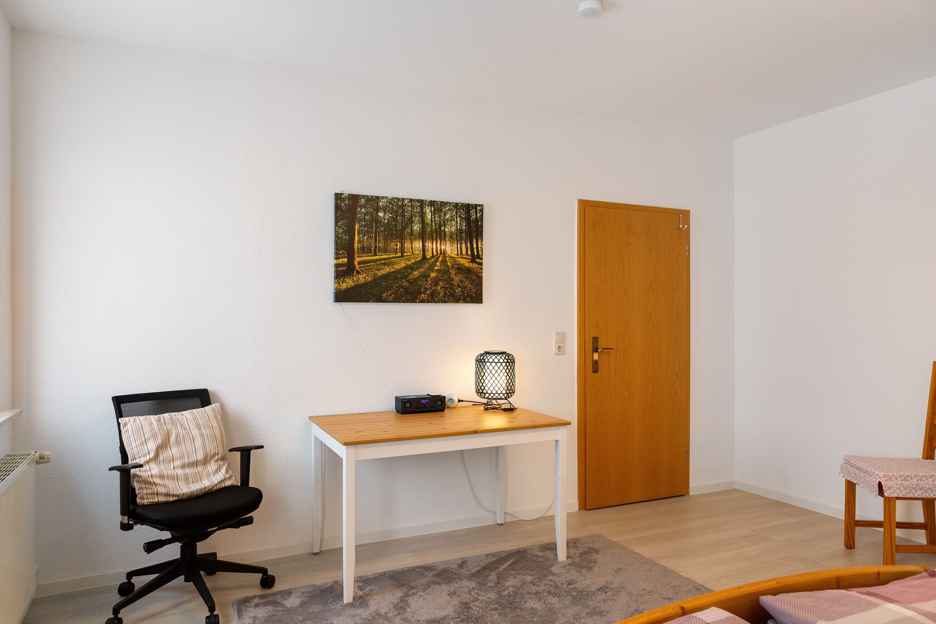 A room with a white desk, a black office chair, a wooden door, and a small table with a chair.