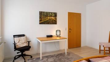 A room with a white desk, a black office chair, a wooden door, and a small table with a chair.