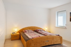 Una cama individual con estructura de madera, dos mesitas de noche con lámparas, una ventana con persianas y una pared de tono claro.