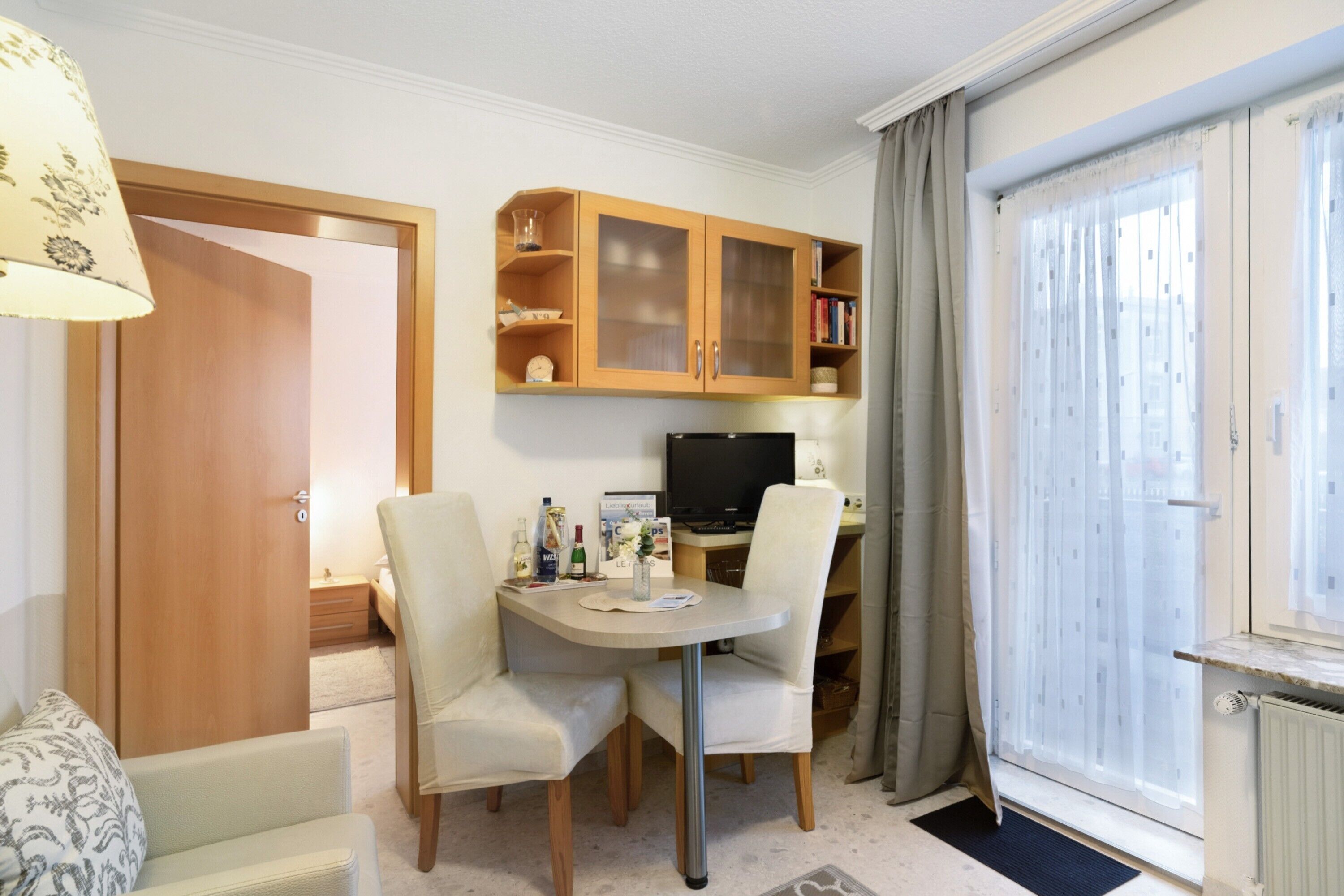 Una habitación con una mesa de comedor, sillas, televisión, un mueble con puertas de vidrio y una ventana con cortinas.