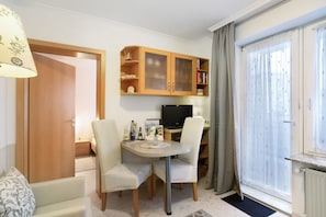 Une pièce comprenant une table à manger, des chaises, un téléviseur, un meuble avec des portes en verre et une fenêtre avec des rideaux.