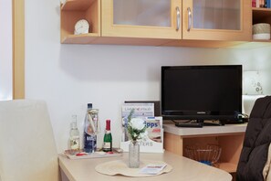 A hotel room with a television, a small table with a tray of snacks, a bottle of wine, a vase with flowers, and a magazine.
