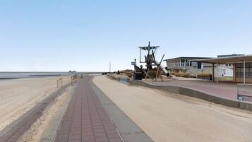 Une promenade en bord de mer avec un sentier de sable, une structure en bois et un bâtiment doté d’une zone abritée.