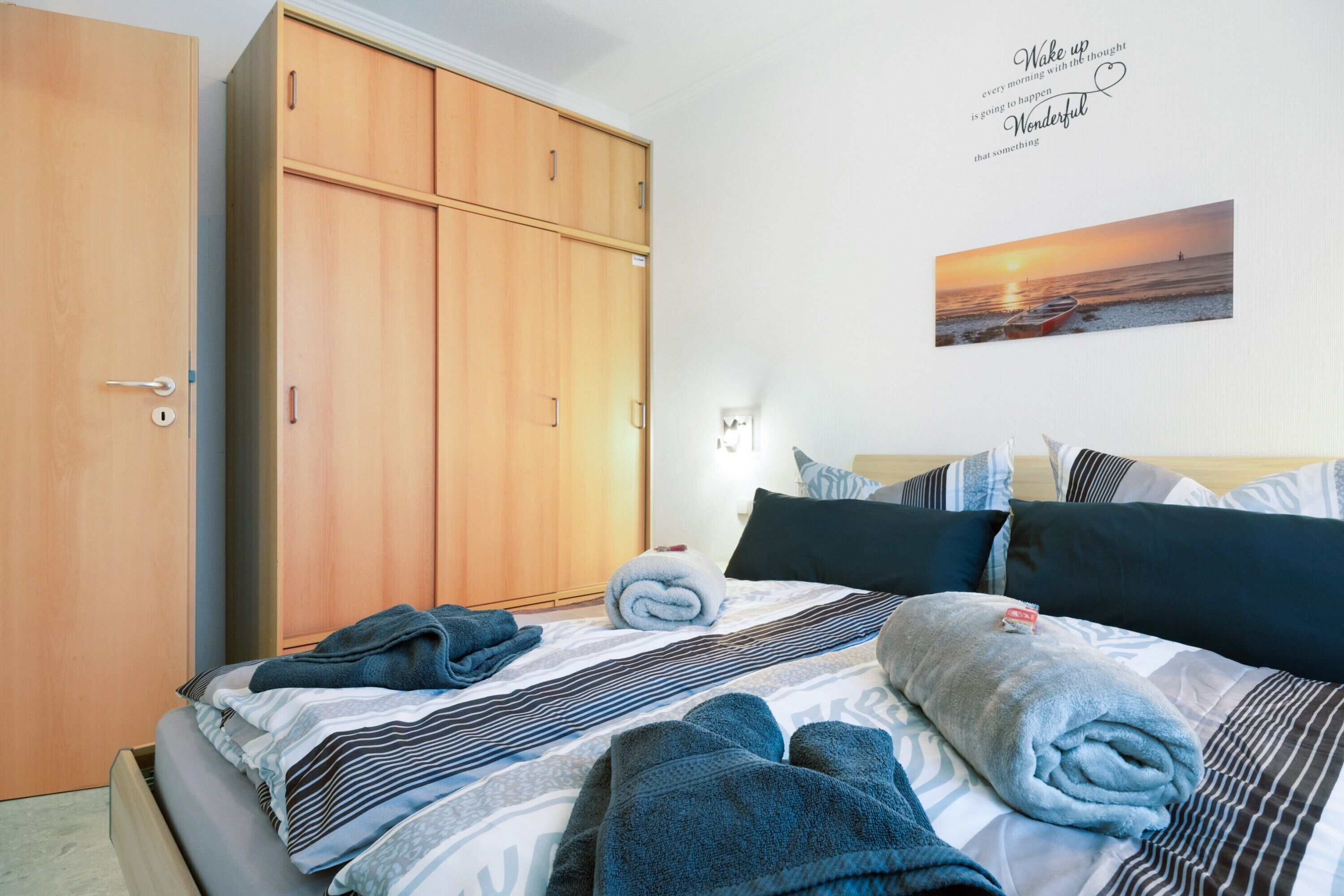 Un dormitorio con cama, armario, una obra de arte de un atardecer y una cita motivacional.