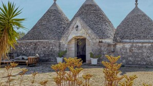 A stone building with three conical roofs, a wooden bench, and potted plants. - TD Trulli Dell Uliveto Cozy Trulli With Pool (Castellana Grotte)