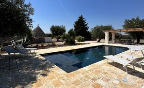 Ein Pool mit Liegestühlen, ein Steinhaus und Bäume.