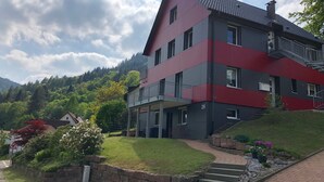 Un immeuble à plusieurs étages, doté d’une façade rouge et grise, d’un balcon et d’un escalier menant à l’entrée.