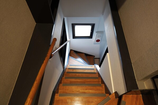 A wooden staircase with a handrail, a small window at the top, and a fire alarm on the wall. - Penthouse 1-bedroom Flat in Hiroo Shibuya (Tokyo)