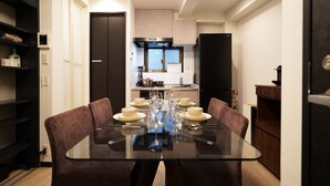A modern dining area with a glass table, brown upholstered chairs, and a kitchen in the background. - Penthouse 1-bedroom Flat in Hiroo Shibuya (Tokyo)