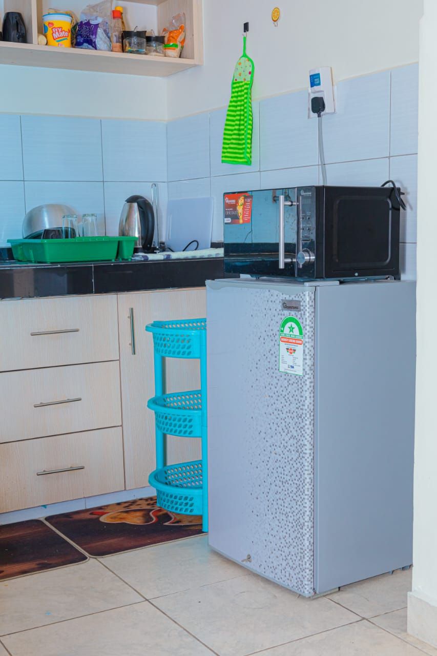 A kitchen with a refrigerator, microwave, and various kitchen items on the counter.