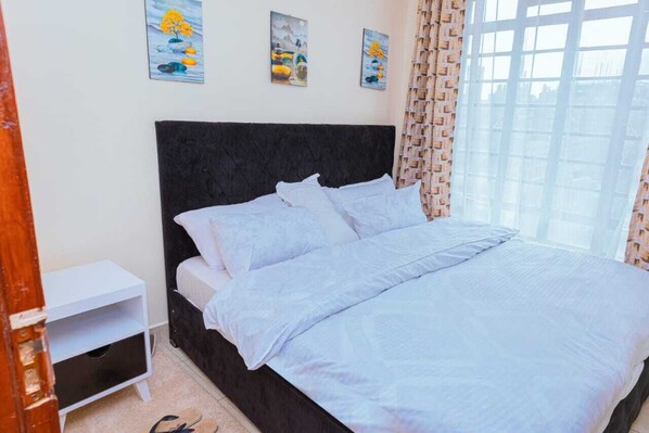A bedroom with a black headboard, white bedding, and three paintings on the wall.