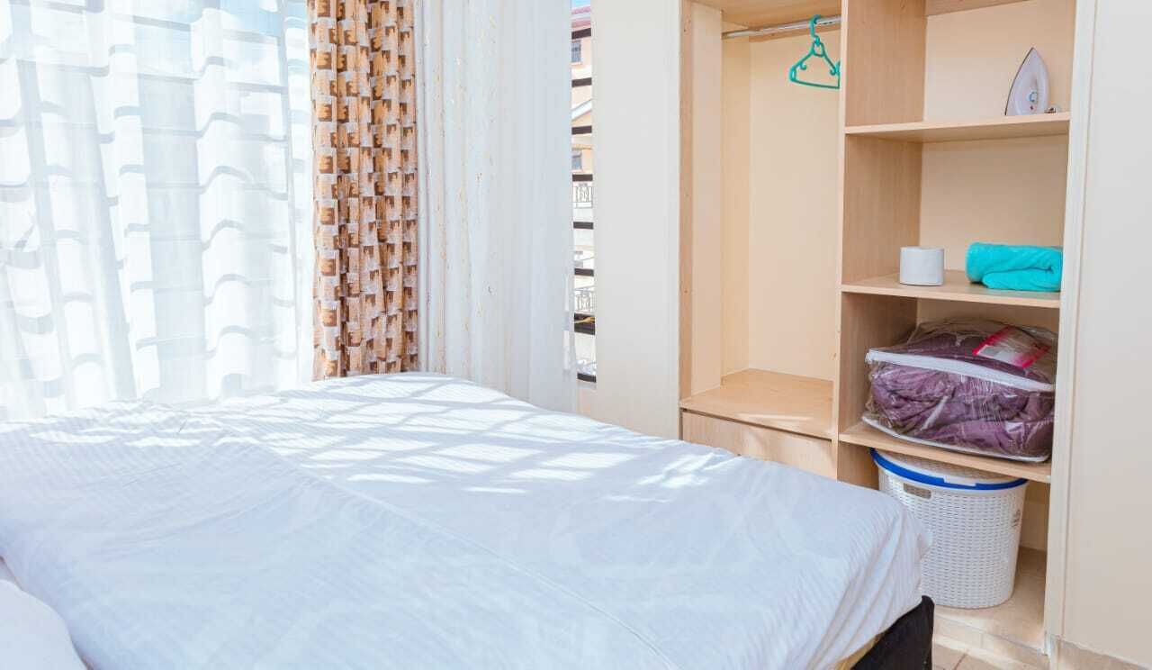 A bedroom with a bed, a wardrobe, a window with curtains, and a laundry basket.