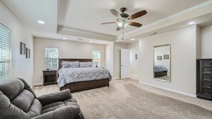 A bedroom with a bed, a ceiling fan, a large mirror, and a gray armchair.