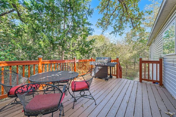 A wooden deck with a barbecue grill, a round table, and two chairs.