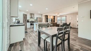 A modern kitchen with a central island, dining area with chairs, and a ceiling fan.