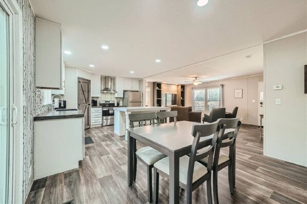 A modern kitchen with a central island, dining area with chairs, and a ceiling fan.