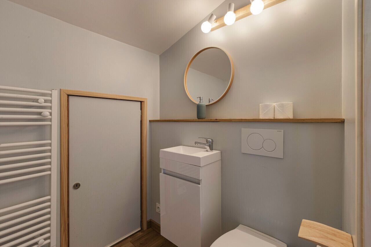 A bathroom with a white sink, a round mirror, and a towel rack.