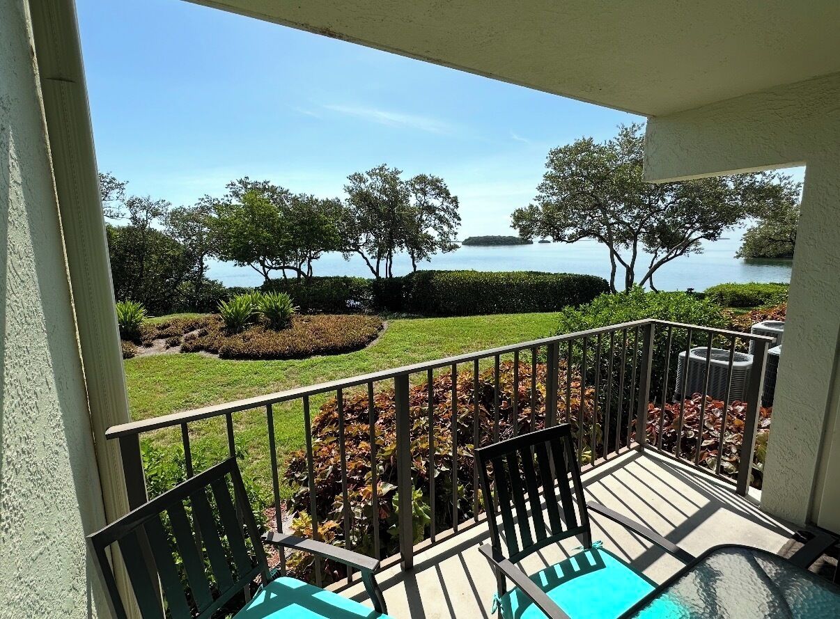 A balcony with a view of a lake, a chair, and a small table.