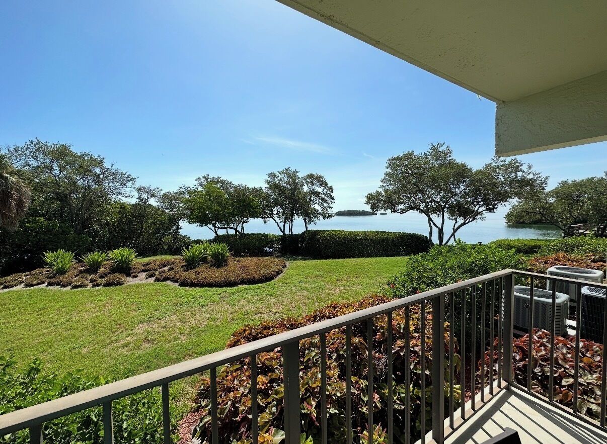 A balcony with a view of a landscaped garden and a body of water.