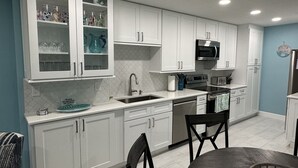 Una cocina moderna con armarios blancos, un microondas de acero inoxidable y un lavabo.