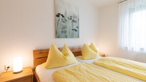 A hotel room with a bed, pillows, a bedside table with a lamp, and a painting on the wall. - Ferienwohnung Chiemsee 72 qm (Rimsting)