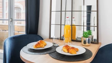 Un coin repas avec une table, des chaises, un miroir et une bouteille de jus d’orange.