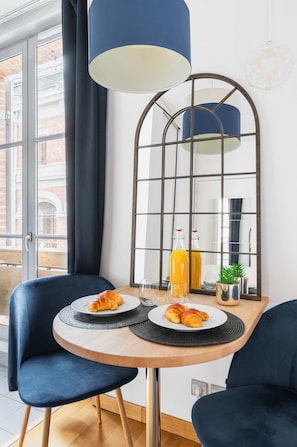 Een eethoek met een tafel, stoelen, een spiegel en een fles sinaasappelsap.