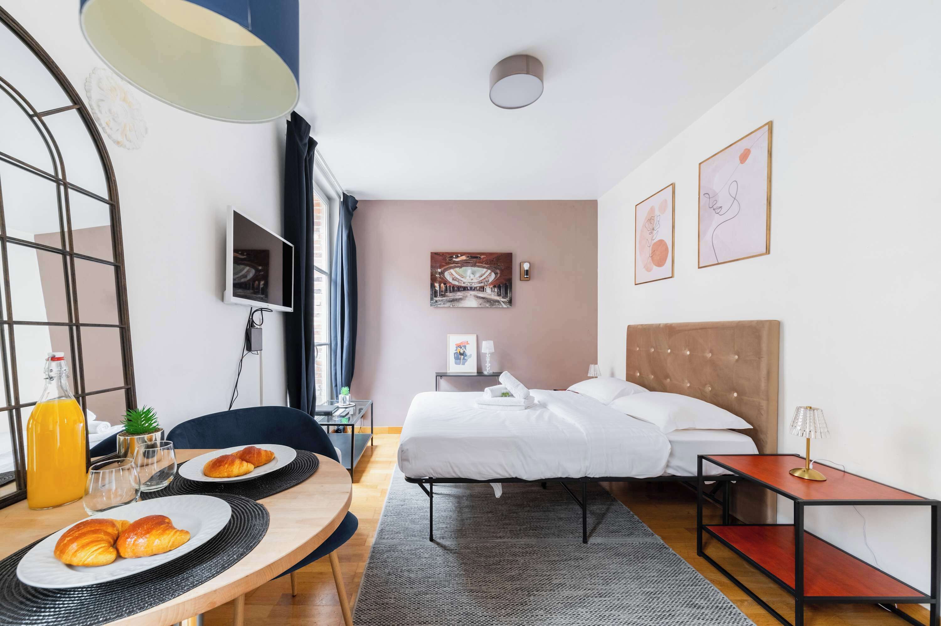 Une chambre d’hôtel équipée d’un lit, d’une table de chevet, d’une lampe, d’œuvres d’art et d’un plateau de petit-déjeuner.