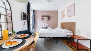 A hotel room with a bed, bedside table, lamp, artwork, and breakfast setup.