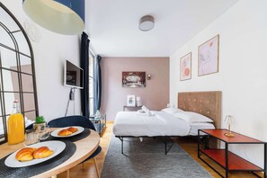 A hotel room with a bed, bedside table, lamp, artwork, and breakfast setup.