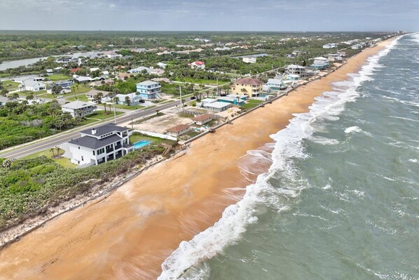 Vista aérea de una zona residencial costera con casas a lo largo de la playa, una carretera y una vista despejada del océano.