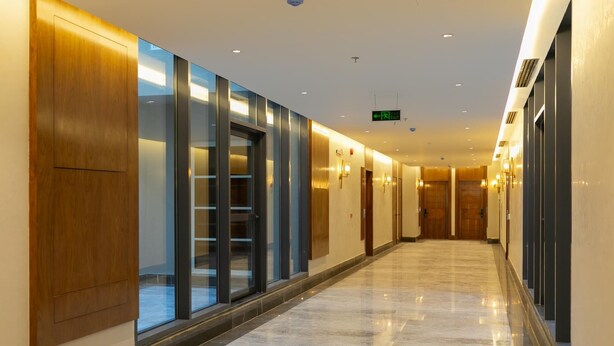 Un corredor de hotel moderno con puertas de vidrio, paneles de madera y un piso de mármol pulido.