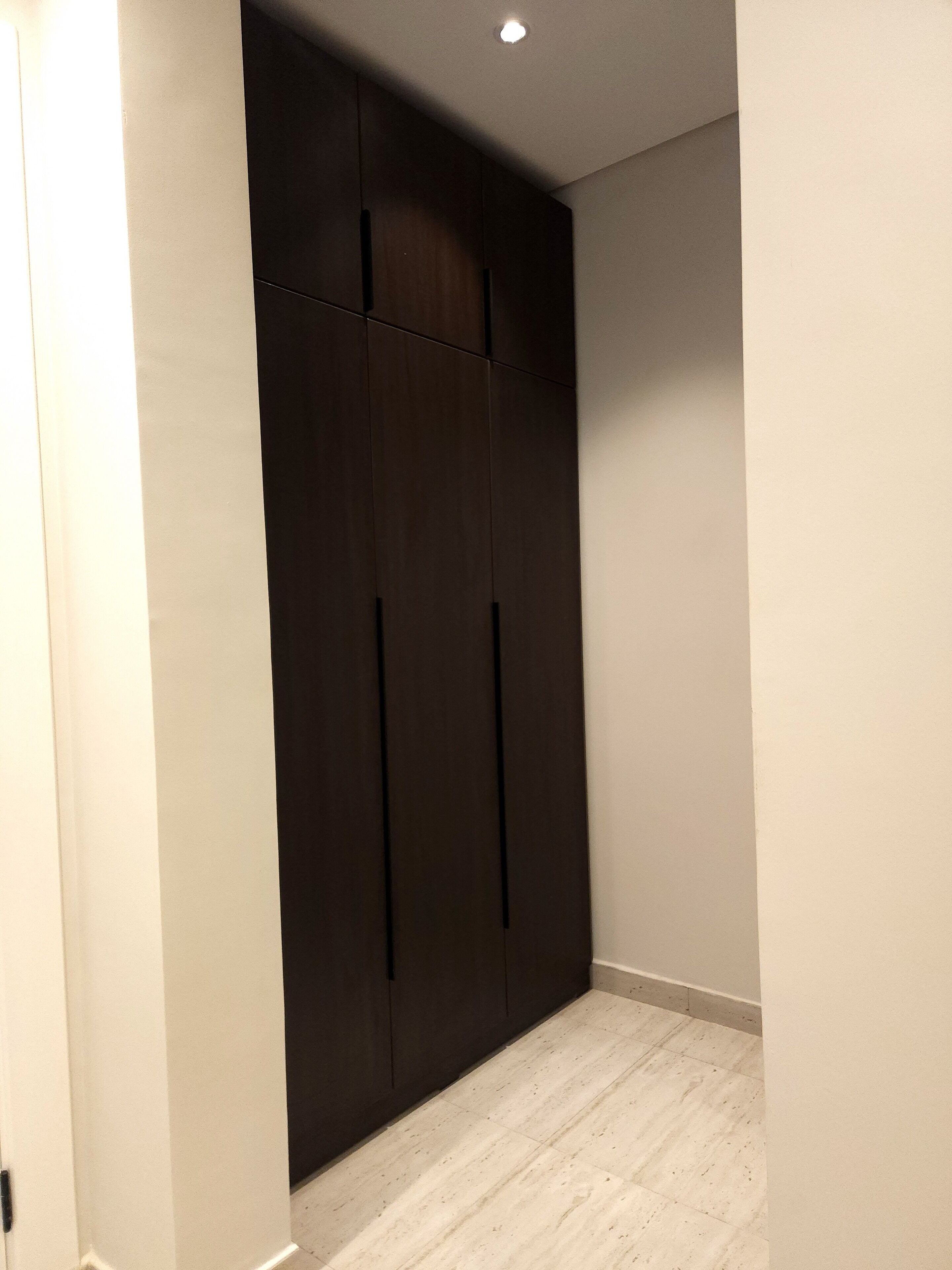 A hallway with a dark wooden wardrobe, light-colored walls, and a tiled floor.