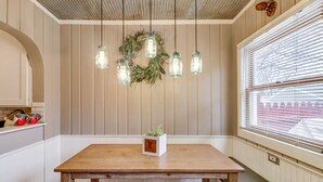 A dining area with a wooden table and chairs, a hanging light fixture with mason jar shades, and a potted plant on the table.