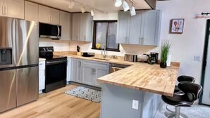A modern kitchen with stainless steel appliances, grey cabinets, and a wooden island with bar stools. - Unique/modern/Mt Si/Shopping (North Bend)