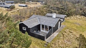 A modern, black-roofed cabin with a large porch and a covered outdoor seating area, surrounded by a natural landscape with sparse trees and a distant view of other cabins. - "Florencia" - 450m from the sea by Interhome (Løkken)
