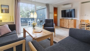 A modern living room with a sofa, armchair, and coffee table. There is a TV mounted on the wall and a dining area with chairs. - "Florencia" - 450m from the sea by Interhome (Løkken)