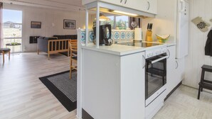 A compact kitchen with white cabinets, a built-in oven, and a coffee maker. There is a dining area with a table and chairs, and a large window providing a view of the outdoors. - "Florencia" - 450m from the sea by Interhome (Løkken)