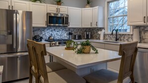 Una cocina moderna con armarios blancos, electrodomésticos de acero inoxidable y una isla central con asientos.