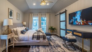 Un dormitorio moderno con cama, mesitas de noche, televisor y un amplio ventanal.