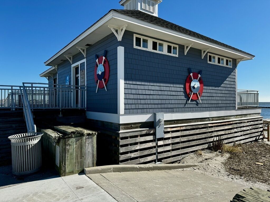 A lifeguard station with a blue exterior, two lifebuoys, a trash can, and a wooden fence.